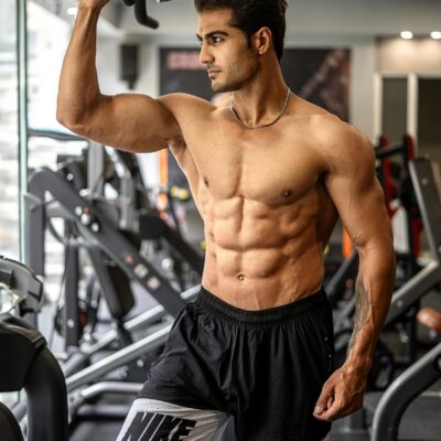 Muscular man standing shirtless in a gym, engaging in a workout with state-of-the-art equipment.