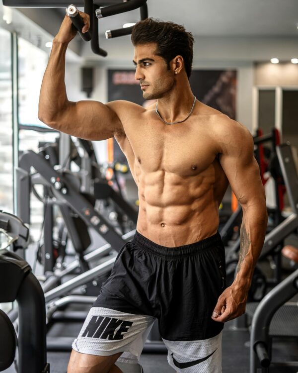 Muscular man standing shirtless in a gym, engaging in a workout with state-of-the-art equipment.