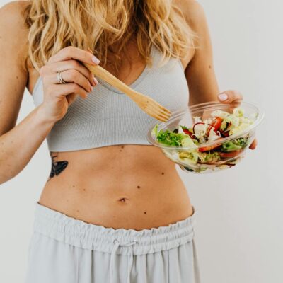 Young woman in sports attire holding a fresh salad bowl, promoting a healthy lifestyle.