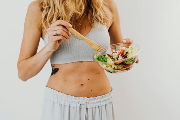 Young woman in sports attire holding a fresh salad bowl, promoting a healthy lifestyle.